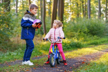 Erkek kardeş, kız kardeş, kız kardeş bisiklet kaskını kafasına taktı. Kardeş mutlu çocuk bisikleti öğretiyor ve bisikletle eğleniyor. Aktif aile fertleri açık havada. Çocuk aktivitesi.