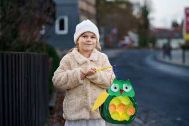 Little preschool kid girl holding selfmade traditional owl lanterns with candle for St. Martin procession. child happy about children and family parade in kindergarten. German tradition Martinsumzug. clipart