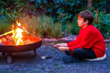 Genç çocuk yaz kampında kızarmış ekmek çubuğunu ateşe veriyor. Mutlu çocuk tatillerini spor kampında geçiriyor.
