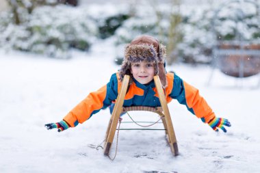 Küçük çocuk kar yağışı sırasında kızak sürmekten hoşlanıyor. Eski model kızakla gezen mutlu anaokulu çocuğu. Çocuk dışarıda karla oynuyor. Kışın aile Noel tatili için aktif eğlence.