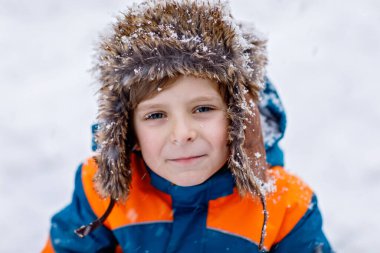 Renkli giysiler içinde kar yağarken dışarıda oynayan komik küçük okul çocuğu. Soğuk karlı günlerde, kışın çocuklarla aktif eğlence. Mutlu çocuk eğleniyor ve karla oynuyor.