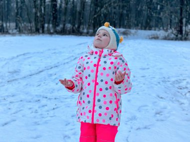 Güzel Kış Parkı 'nda Eğlenen Komik Küçük Kız. Karla oynayan mutlu okul çocuğu, kar ve kış aktiviteleriyle ilgili mutluluk.