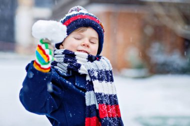 Renkli kış kıyafetleri içinde, kar yağarken dışarıda oynayıp eğlenen sevimli, komik bir çocuk. Çocuklarla açık hava eğlencesi. Çocuk ve bebek kartopu savaşı yapıyor.