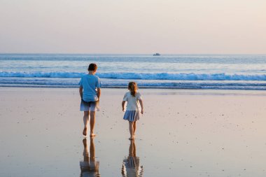 Üç çocuk, gün batımında okyanus sahilinde mutlu kardeşler. Mutlu bir aile, iki okul çocuğu ve küçük bir anaokulu kızı. Kardeşler eğleniyor, İspanya, Costa del Sol