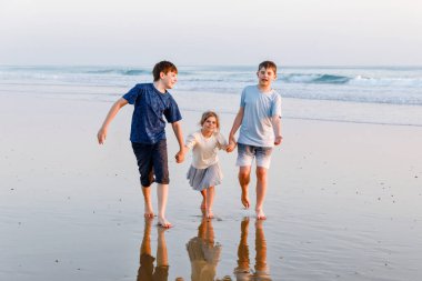 Üç çocuk, gün batımında okyanus sahilinde mutlu kardeşler. Mutlu bir aile, iki okul çocuğu ve küçük bir anaokulu kızı. Kardeşler eğleniyor, İspanya, Costa del Sol