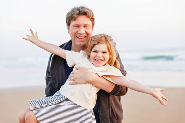 Sağlıklı bir baba ve kızı gün batımında kumsalda birlikte oynuyorlar. Mutlu bir aile, aşkım. Anaokulu kızı ve orta yaşlı adamın kucaklaşması. Ebeveynler ve çocuklar arasında mutlu bir ilişki