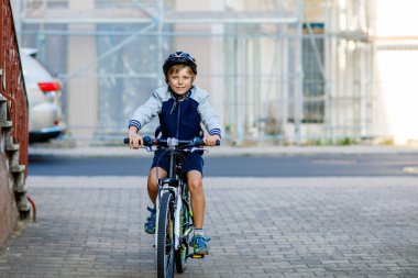 Kasklı liseli çocuk şehirde sırt çantasıyla bisiklet sürüyor. Renkli elbiseli mutlu çocuk okula giderken bisiklete biniyor. Çocuklar için güvenli okul yolu..