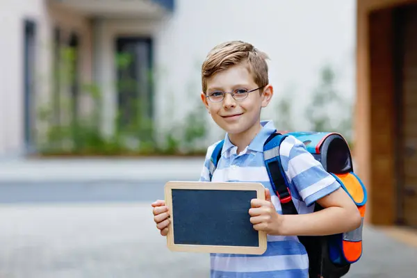 stock image Happy little kid boy with backpack or satchel. Schoolkid on the way to school. Healthy adorable child outdoors With chalk desk for copyspace. Back to school or schools out