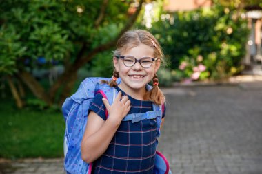 Gözlüklü, sırt çantalı, çantalı ve okulun ilk günü büyük çantalı mutlu bir kız çocuğu. Dışarıda sağlıklı, sevimli bir çocuk var. Okula geri dön..