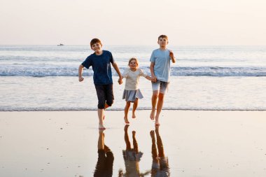 Üç çocuk, gün batımında okyanus sahilinde mutlu kardeşler. Mutlu bir aile, iki okul çocuğu ve küçük bir anaokulu kızı. Kardeşler eğleniyor, İspanya, Costa del Sol