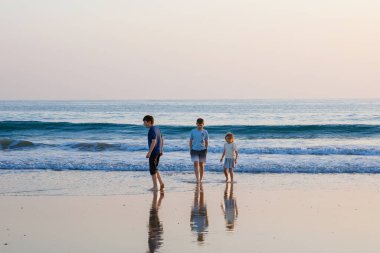 Üç çocuk, gün batımında okyanus sahilinde mutlu kardeşler. Mutlu bir aile, iki okul çocuğu ve küçük bir anaokulu kızı. Kardeşler eğleniyor, İspanya, Costa del Sol