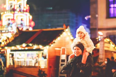 Almanya 'da Noel pazarında babasının omzunda oturan küçük bir anaokulu kızı. Mutlu çocuk ve adam geleneksel dekore edilmiş piramidi izliyor. Mutlu aile, kaynaşma, aşk. Aile Xmas zamanı