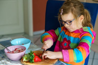 Littl anaokulu bıçak kullanmayı öğreniyor çilek kesmeyi mutfakta kahvaltıda yulaf lapası yapmak için meyve salatası yapmayı. Çocuklar için sağlıklı yiyecekler