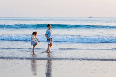 Okyanus sahilinde iki çocuk. Ergen çocuk ve anaokulu kız kardeşi gün batımında eğleniyorlar. Aile için deniz tatili. Kardeşler gülüyor ve gülüyor. Mutluluk ve aşk