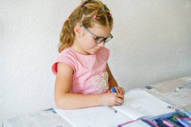 Masada oturan gözlüklü genç bir kız çalışma kitabına yazmaya odaklanmış. Çocuk kurşun kalemle numara yazıyor, öğrenmekle meşgul. İlkokul, eğitim