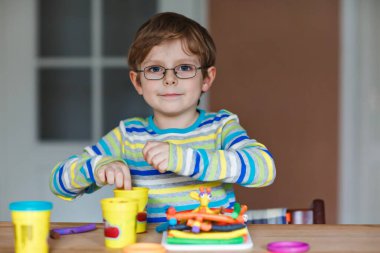Gülümseyen anaokulu çocuğu hamurla eğleniyor, renkli modelleme bileşik kiliyle. Çocuklarla yaratıcı bir eğlence. Corona virüsü karantinası sırasında evde kalmak. Sığınma yeri, tecrit kavramı