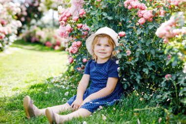 Çiçek açan gül bahçesinde küçük bir kızın portresi. Yaz güneşli bir günde parkta güllerle ve çiçeklerle eğlenen sevimli güzel bir çocuk. Mutlu gülümseyen bebek