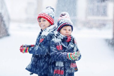 Renkli kıyafetleri olan iki küçük çocuk şiddetli kar yağışı sırasında dışarıda oynuyorlar. Soğuk günlerde kışın çocuklarla aktif bir eğlence. Mutlu kardeşlerim ve arkadaşlarım ilk karla eğleniyorlar.
