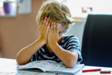 Evdeki mutfakta ev ödevi yapan yorgun çocuğun portresi. İlköğretim okulunda yazma ve öğrenme üzerine çalışıyorum. Üzgün ve öfkeli çocuk.