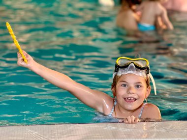 Happy little girl with in swimming pool learning to dive. Little school child with swimm glasses, picking things from pool bottom. Healthy sport activity and fun for children clipart