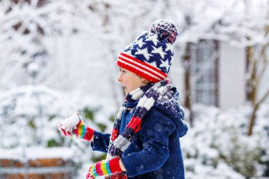 Renkli elbiseli anaokulu çocuğu şiddetli kar yağışı sırasında dışarıda oynuyor. Soğuk karlı günlerde, kışın çocuklarla aktif eğlence. Mutlu çocuk eğleniyor, karla oynuyor. Kış modası