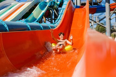 Açık deniz parkında oynayan genç bir çocuk. Genç, aile tatillerinde Aquapark 'ta şişme lastik çemberde kayarken eğleniyor.