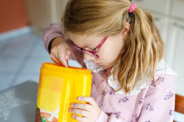 Mutfak masasında sıcak çikolata karıştıran, pembe çiçekli süveter ve gözlük takan, rahat ev atmosferi, sabah ya da kış içeceği hazırlayan, sıcak ve rahatlatıcı bir sahne. Çocuk eğleniyor..