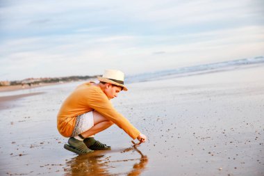 Mutlu neşeli genç gün batımında sahilde duruyor. Küçük çocuk kameraya gülümsüyor. Çocuk denizde aile tatiline çıktı.