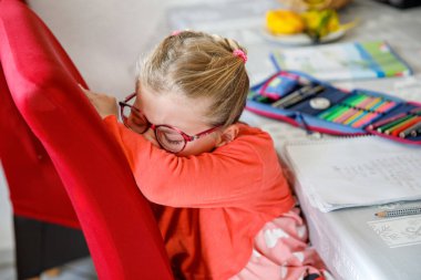 Küçük liseli kız üzgün ve üzgün, elleriyle yüzünü örtüyor. Okul kızı ödevlerini yaparken ağlıyor.