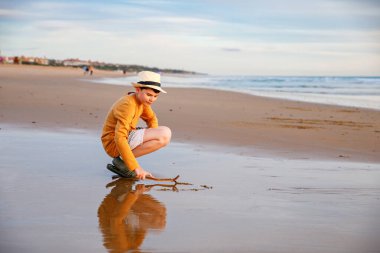 Mutlu neşeli genç gün batımında sahilde duruyor. Küçük çocuk kameraya gülümsüyor. Çocuk denizde aile tatiline çıktı.