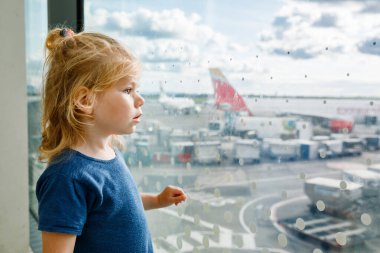 Havaalanında küçük tatlı bir kız, seyahat ediyor. Pencerenin yanında bekleyen ve uçakları izleyen mutlu sağlıklı çocuk. Aile uçakla yaz tatiline çıkıyor.