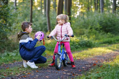 Erkek kardeş, kız kardeş, kız kardeş bisiklet kaskını kafasına taktı. Kardeş mutlu çocuk bisikleti öğretiyor ve bisikletle eğleniyor. Aktif aile fertleri açık havada. Çocuk aktivitesi.