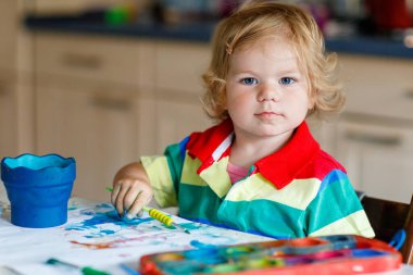 Sulu boyayla resim yapmayı öğrenen sevimli bir bebek. Evde renkli fırçalar kullanarak resim çizen küçük bir çocuk. Sağlıklı, mutlu, renkler, su ya da çocuk odası deneyleri yapan bir kız.