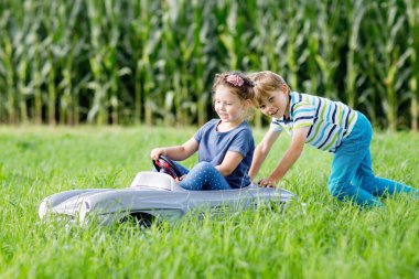 İki mutlu çocuk açık havada, yaz bahçesinde eski oyuncak arabalarıyla oynuyorlar. İçinde küçük bir kız olan arabayı süren bir çocuk. Gülen ve gülümseyen çocuklar. Aile, çocukluk, yaşam tarzı konsepti.