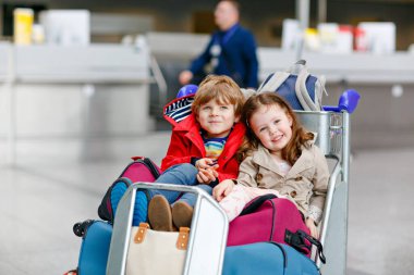 İki küçük çocuk, erkek ve kız, havaalanında ikiz kardeşler. Mutlu çocuklar, birlikte seyahat eden aile, uçakla tatile gitmek ve terminalde bavullarla beklemek.