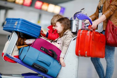 İki küçük çocuk, erkek ve kız, kardeşler ve anne havaalanında. Çocuklar, aile seyahati, uçakla tatile gitmek ve bir kadının terminalden uçmak için ittiği valizlerle tramvayda beklemek.