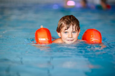 Active adorable little preschool kid boy with swimmies learning to swim in an indoor pool. Active and fit leisure for children. Happy child making sports and learning safe swimming. clipart