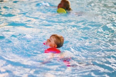 Active adorable little preschool kid boy with swimmies learning to swim in an indoor pool. Active and fit leisure for children. Happy child making sports and learning safe swimming. clipart