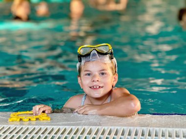 Happy little girl with in swimming pool learning to dive. Little school child with swimm glasses, picking things from pool bottom. Healthy sport activity and fun for children clipart