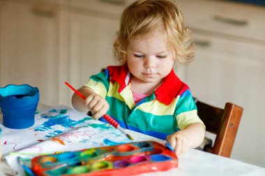 Sulu boyayla resim yapmayı öğrenen sevimli bir bebek. Evde renkli fırçalar kullanarak resim çizen küçük bir çocuk. Sağlıklı, mutlu, renkler, su ya da çocuk odası deneyleri yapan bir kız.