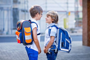 Çantalı iki küçük çocuk. Okulun yolu üzerindeki okul çocukları. Sağlıklı çocuklar, erkek kardeşler ve en iyi arkadaşlar sokakta evden ayrılıyorlar. Okula dönelim. Mutlu kardeşler..