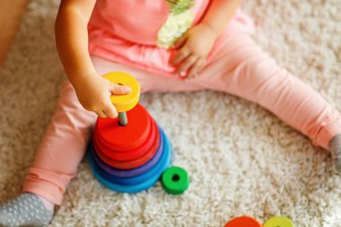 Close-up of toddler sits on a carpet, playing with colorful wooden rings and a toy truck, focused on stacking the pieces. Child plays with rainbow colored pyramid at home or nursery. clipart