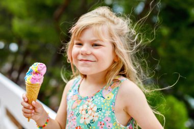 Güneşli yaz gününde krep külahında renkli dondurma yiyen mutlu anaokulu kızı. Küçük çocuk dondurmalı tatlı yiyordu. Sıcak yaz günlerinde tatlı yiyecekler. Parlak ışık, renkli dondurma..