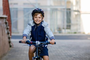 Kasklı liseli çocuk şehirde sırt çantasıyla bisiklet sürüyor. Renkli elbiseli mutlu çocuk okula giderken bisiklete biniyor. Çocuklar için güvenli okul yolu..