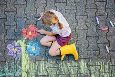 Sevimli küçük kız ve asfalta renkli tebeşirle boyanmış çiçekler. Mutlu anaokulu çocuğu tebeşirle resim yaparken eğleniyor. Çocuklar için yaratıcı eğlence, çizim ve resim