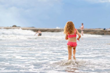 Mutlu çocuk, egzotik plajlarda yaz tatili sırasında mayo giymiş koşan ve dalgalarda zıplayan küçük anaokulu kızı. Okyanus Kıyısındaki Aile Seyahati