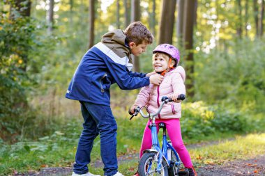 Erkek kardeş, kız kardeş, kız kardeş bisiklet kaskını kafasına taktı. Kardeş mutlu çocuk bisikleti öğretiyor ve bisikletle eğleniyor. Aktif aile fertleri açık havada. Çocuk aktivitesi.