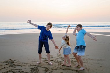 Three children, happy siblings on ocean beach at sunset. happy family, two school boys and one little preschool girl. Brothers and sister having fun, Spain, Costa del Sol clipart