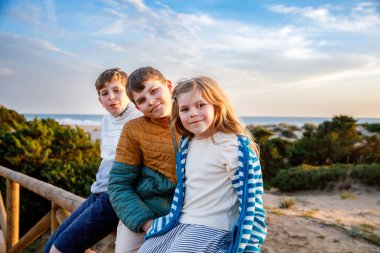 Portrait of three children, happy kids on beach at sunset. happy family, two school boys and one little preschool girl. Siblings having fun together. Bonding and family vacation. clipart