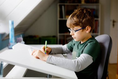 Gözlüklü çocuk okul için evde öğreniyor. Çocuk ödevini yapıyor.